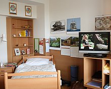 Zimmer des Hufeland-Hauses mit Pflegebett, TV-Schrank, Wandschrank und Nachttisch, im Hintergrund Kalender und einige persönliche Gegenstände