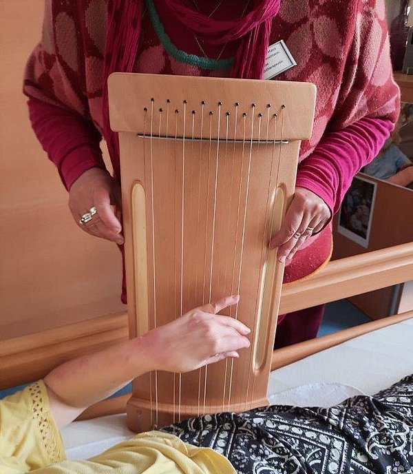 Eine Bewohnerin spielt auf einem Saiteninstrument, das von einer Mitarbeiterin gehalten wird