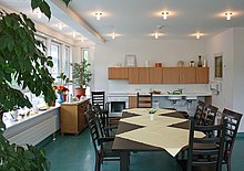 Heller Aufenthaltsraum des Hufeland-Hauses, mit Fenstern und vielen Deckenlampen, in der Mitte ein langer Tisch mit Stühlen, im Hintergrund eine Küchenzeile